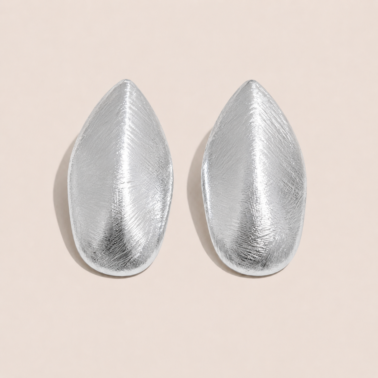 Silver leaf-shaped stud earrings with a brushed textured finish on a cream backdrop — Folie à Trois Foglia EARRINGS
