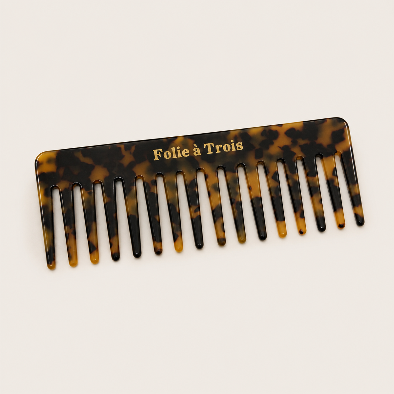 Folie Hair Comb wide-tooth tortoiseshell acetate comb with gold Folie à Trois branding, studio flat-lay on cream.