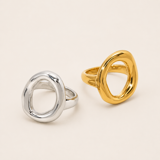 Silver and gold Formentera RING side by side, each an open organic asymmetric loop with a chunky polished band, on a cream backdrop.