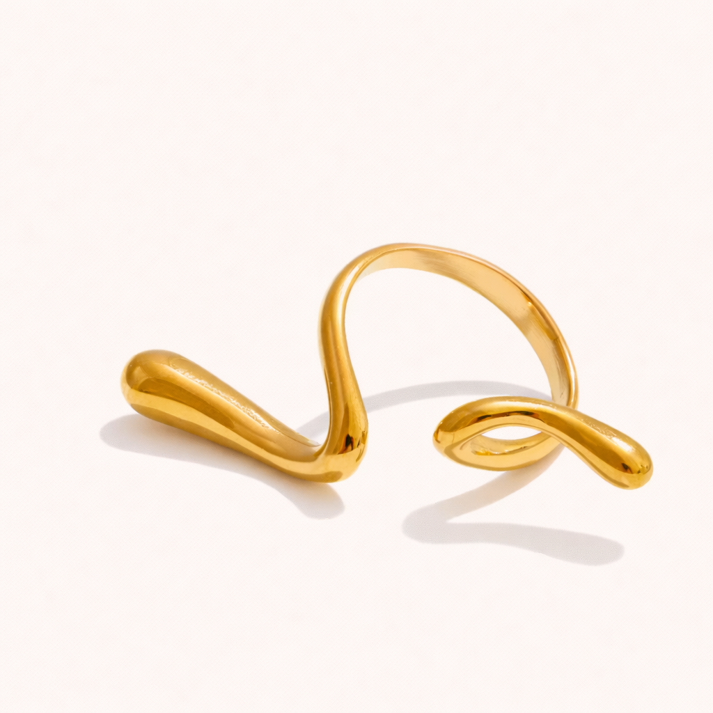 Sculptural gold ring with an asymmetric wavy open design, shown at an angle on a cream backdrop — Frances RING.
