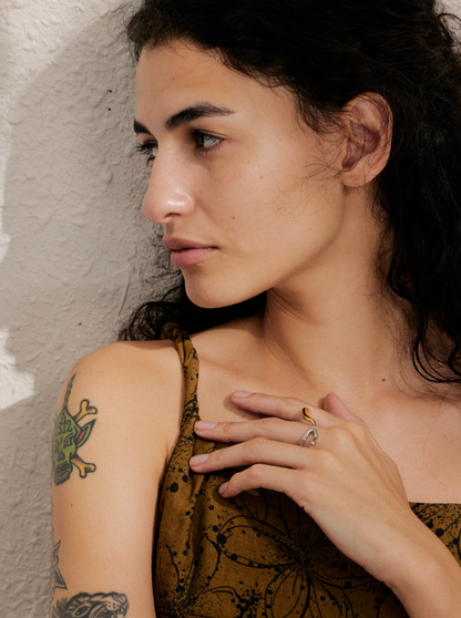 Close-up of a hand near the shoulder wearing the gold Frances RING stacked with a silver hook-shaped ring, tattoo visible.