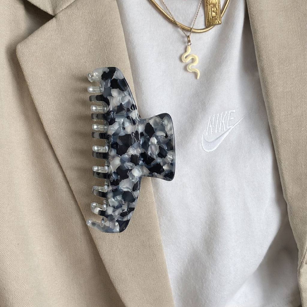 French Girl HAIR CLIP's black and white confetti claw clip pinned to a beige blazer lapel, styled with gold necklaces.