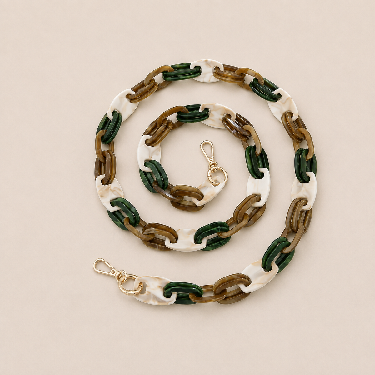 Folie à Trois Frost long wholesale phone chain in white marbled, dark green and brown acetate links with gold clasps, coiled on a cream background.