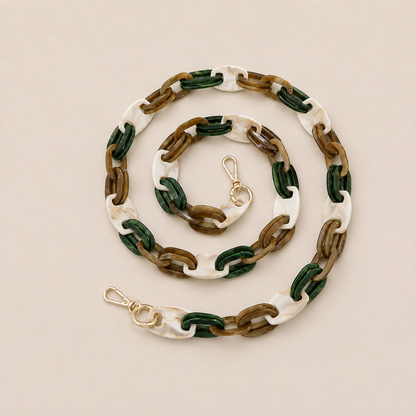 Folie à Trois Frost long wholesale phone chain in white marbled, dark green and brown acetate links with gold clasps, coiled on a cream background.