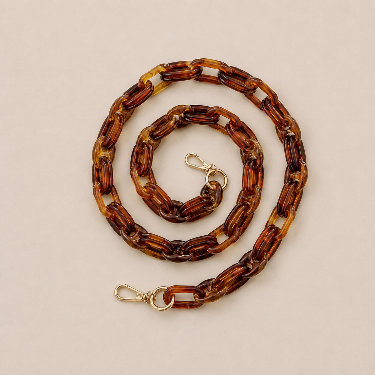 Folie à Trois Frost long wholesale phone chain in tortoiseshell acetate links with gold clasps, coiled on a cream background.