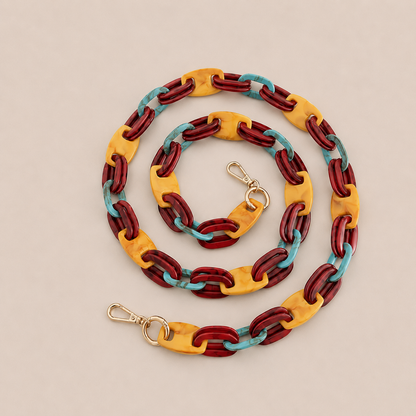 Folie à Trois Frost long wholesale phone chain in burgundy, mustard and turquoise acetate links with gold clasps, coiled on a cream background.