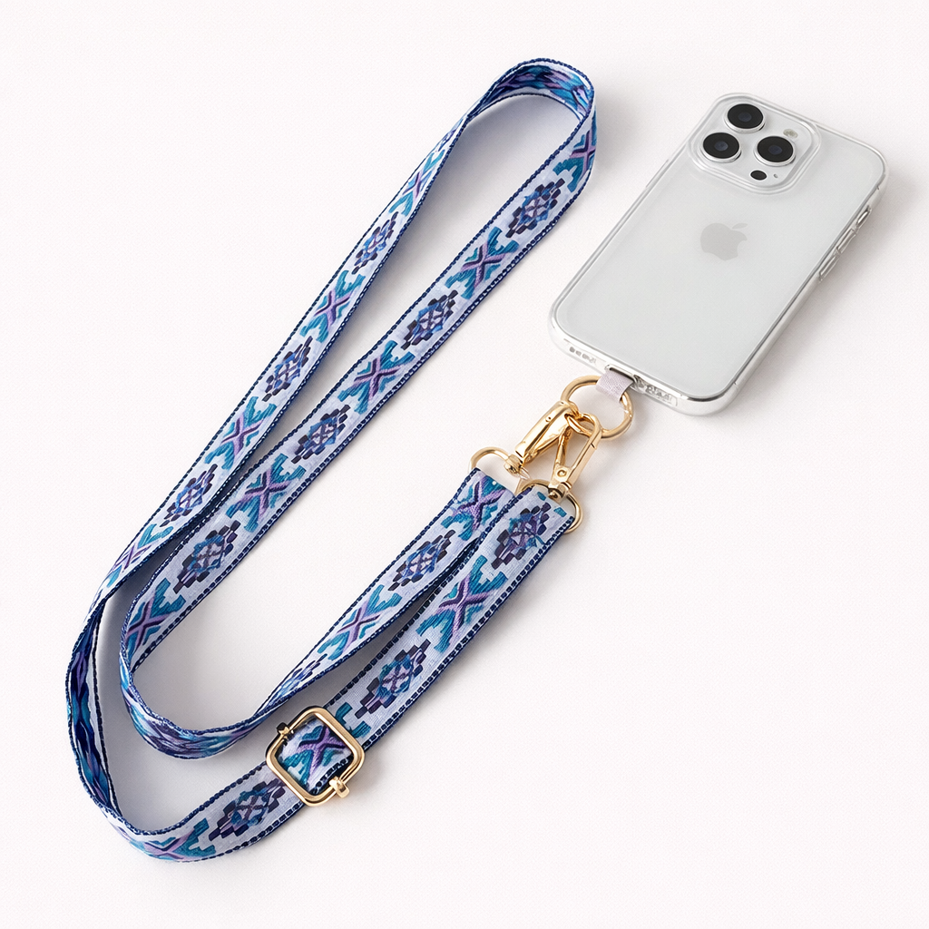 Blue and purple Aztec-pattern Getaway strap laid beside a clear-case phone, gold clasp ready to attach.