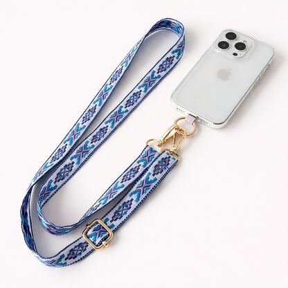 Blue and purple Aztec-pattern Getaway strap laid beside a clear-case phone, gold clasp ready to attach.