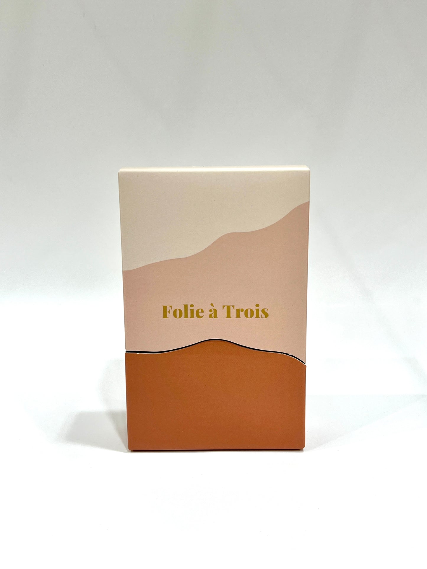 Upright rust and cream Folie à Trois gift box with gold foil branding on a plain white studio background.