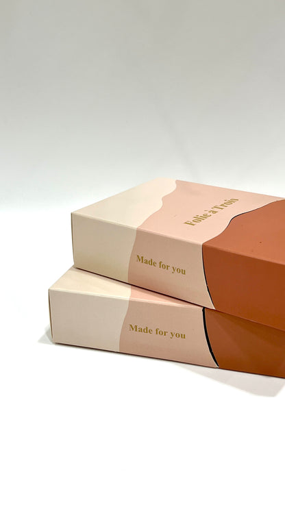 Two stacked rust and cream Folie à Trois gift boxes with made for you text printed along the spine.