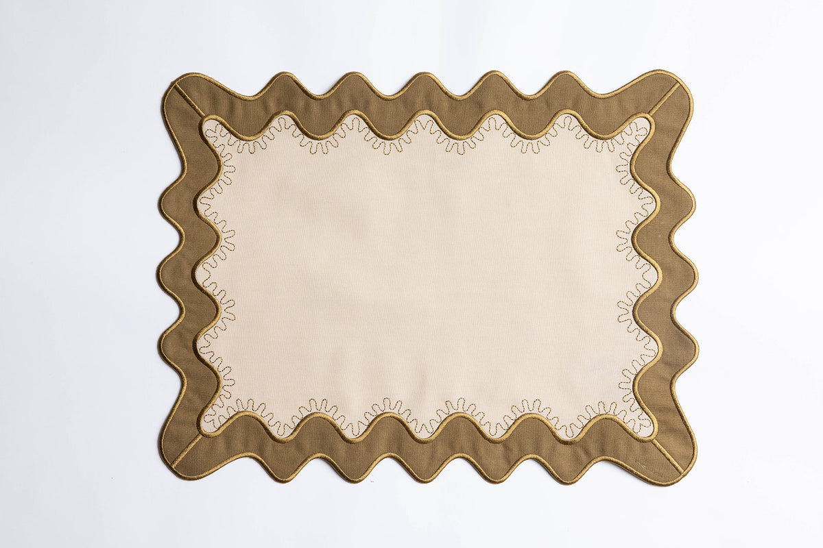 Olive-green scalloped placemat with a cream center and gold-stitched trim, the Gisèle Scallop placemat with embroidered detail.