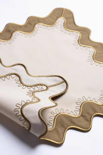 Close-up of a folded olive-green corner with gold-stitched scalloped trim on the Gisèle Scallop placemat with embroidered detail.