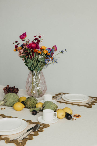 Styled brunch table with fresh flowers, fruit, and white plates set on the olive Gisèle Scallop placemat with embroidered edging.