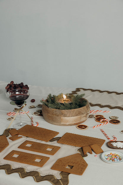 Festive tablescape with wine, a candle, and gingerbread pieces styled beside the olive Gisèle Scallop placemat with embroidered edging.
