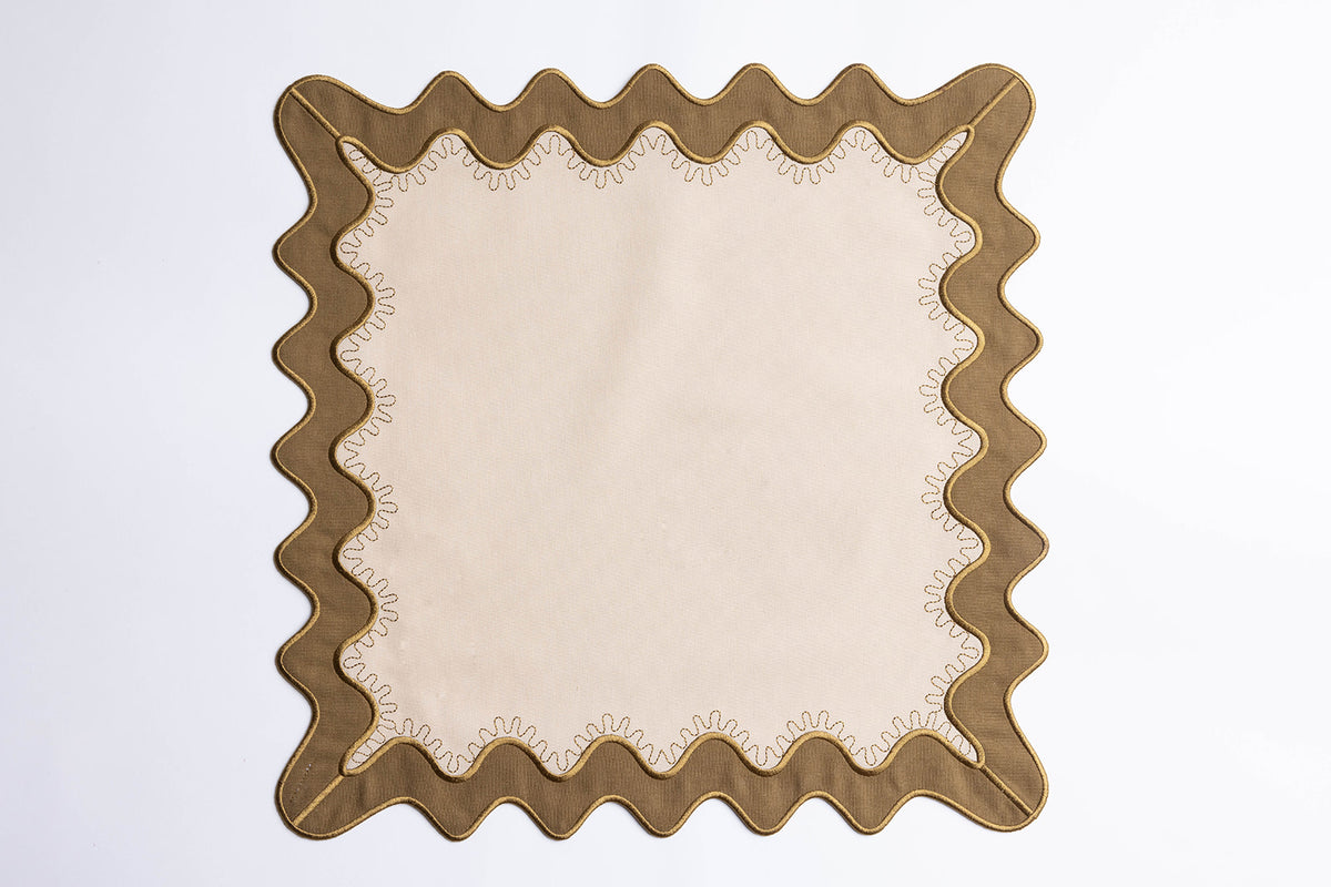 Flat lay of a square cream napkin with an olive scalloped border and gold embroidered stitching, the Gisèle Scallop napkin design.
