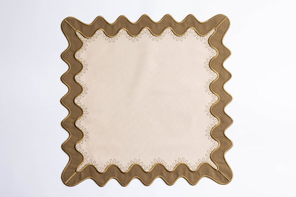 Flat lay of a square cream napkin with an olive scalloped border and gold embroidered stitching, the Gisèle Scallop napkin design.