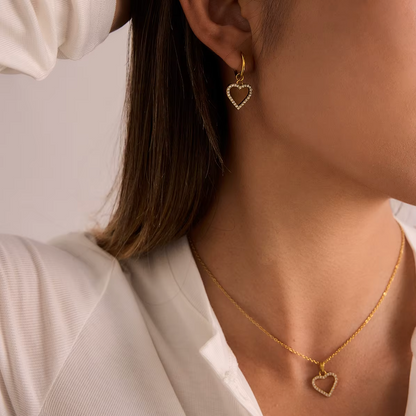 The Golden Heart NECKLACE worn alongside a matching pave heart earring, both pieces catching the light at the neckline.
