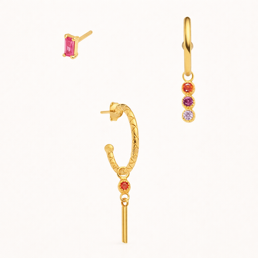 The Gretta SET in gold with pink, red, and purple stones, featuring a baguette stud, a bar-dangle hoop, and a three-stone hoop in studio.