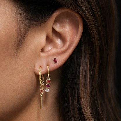 A close-up of a model wearing the Gretta SET in gold, showing the pink baguette stud and two dangle hoops along the ear.