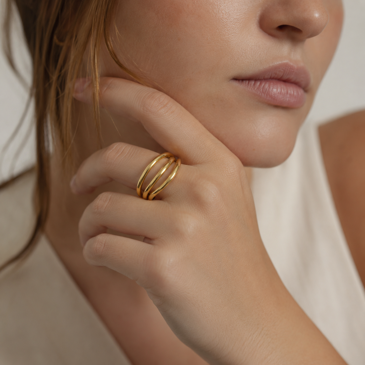 Close-up of a hand near the chin wearing the gold Harley RING with its three interlocking smooth bands.