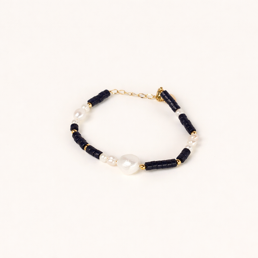 Harlyn BRACELET black beaded bracelet with pearl accents and a large pearl centerpiece, studio flat-lay on cream.