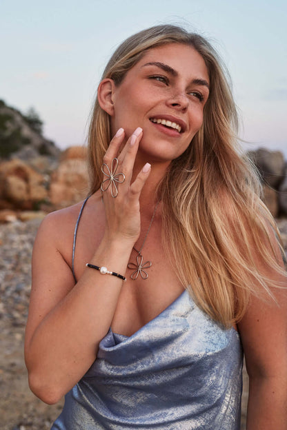 Harlyn BRACELET worn on the wrist, model smiling on a rocky coastal path with a silver flower ring and necklace.