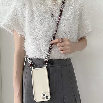 Model wears a black braided Havana phone cord crossbody, holding a cream phone case at the hip.