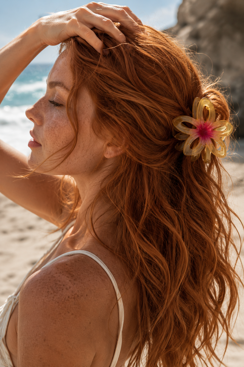 Hawaii HAIR CLIP worn in wavy red hair, yellow flower clip, model at the beach with hand raised.