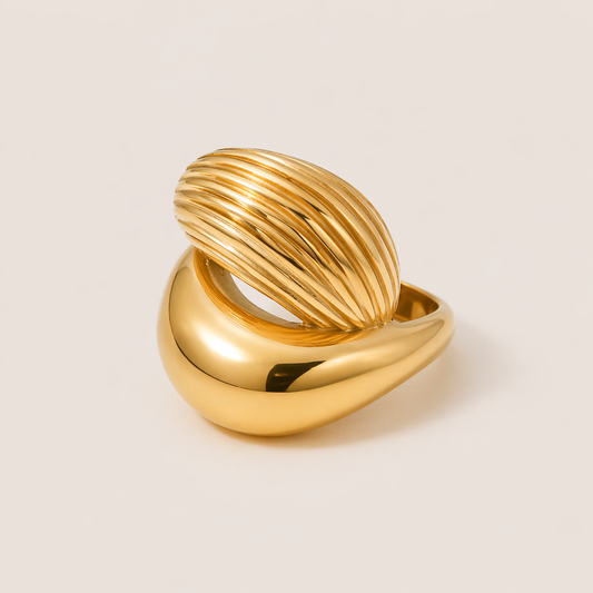 Gold ring split between a smooth polished dome and a fluted ribbed dome, shown in close-up on a cream backdrop — Folie à Trois Hayden RING.