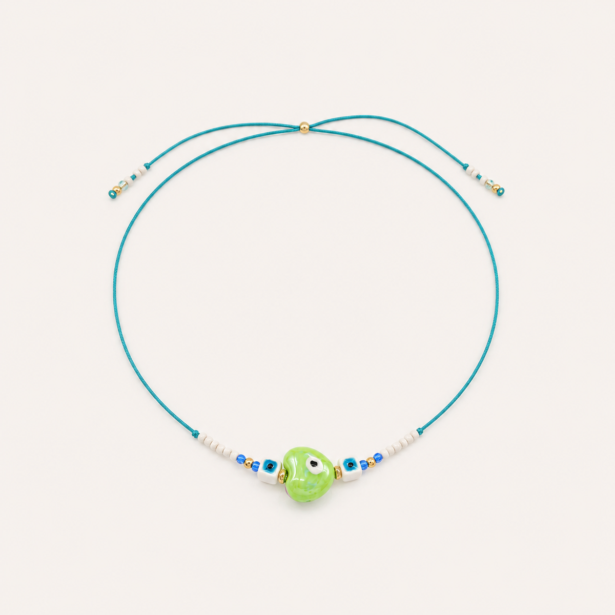 Teal cord Heart Eye NECKLACE with beaded white and blue accents around a green enamel evil eye charm, laid flat.