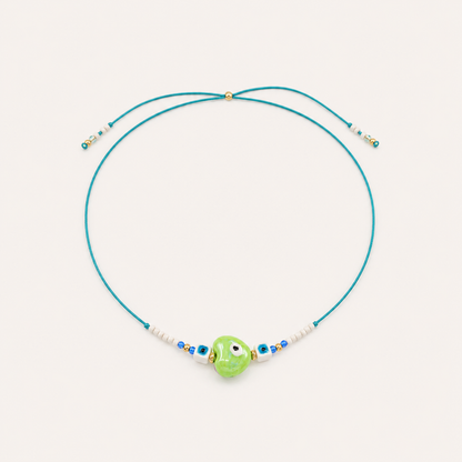 Teal cord Heart Eye NECKLACE with beaded white and blue accents around a green enamel evil eye charm, laid flat.