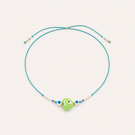 Teal cord Heart Eye NECKLACE with beaded white and blue accents around a green enamel evil eye charm, laid flat.