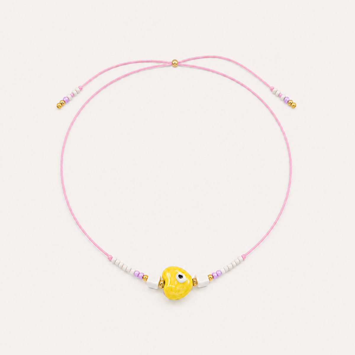 Pink cord Heart Eye NECKLACE with beaded white and lilac accents around a yellow enamel evil eye charm, laid flat.