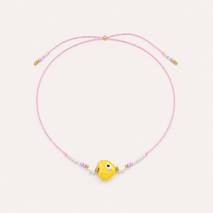 Pink cord Heart Eye NECKLACE with beaded white and lilac accents around a yellow enamel evil eye charm, laid flat.