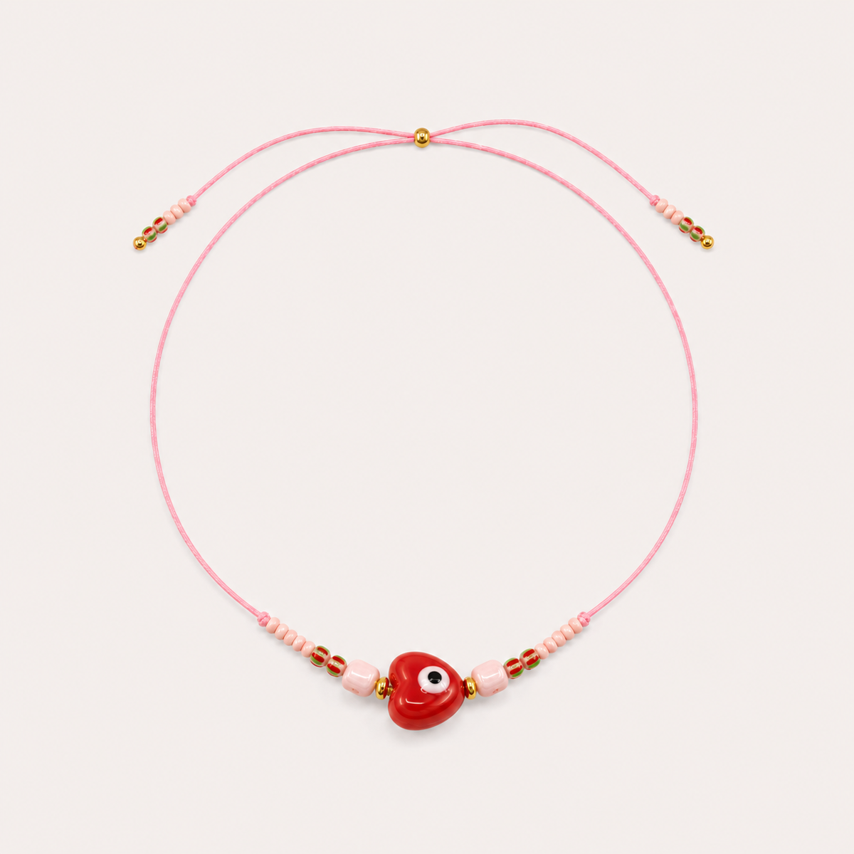 Pink cord Heart Eye NECKLACE with beaded pink and red accents around a red enamel heart-shaped eye charm, laid flat.