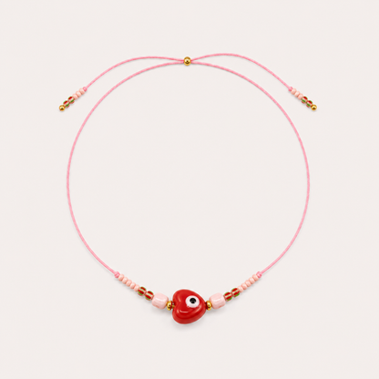 Pink cord Heart Eye NECKLACE with beaded pink and red accents around a red enamel heart-shaped eye charm, laid flat.