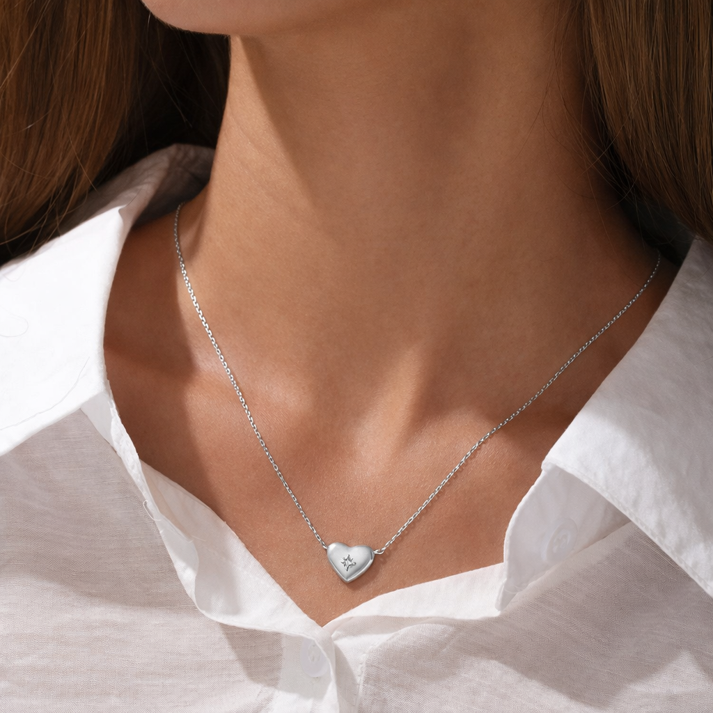 The Heart Me NECKLACE in silver worn at the neckline, the puffed heart pendant resting above a white button-up shirt.