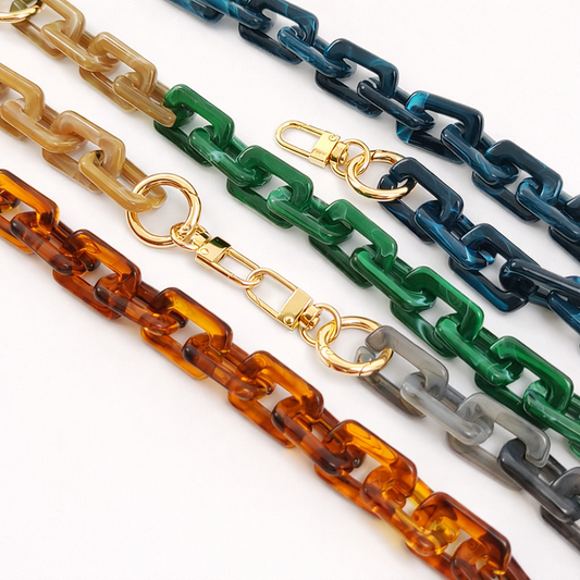 Five acrylic paperclip-link phone chains in cream, navy, green, tortoiseshell, and grey, laid out together with gold clasps.