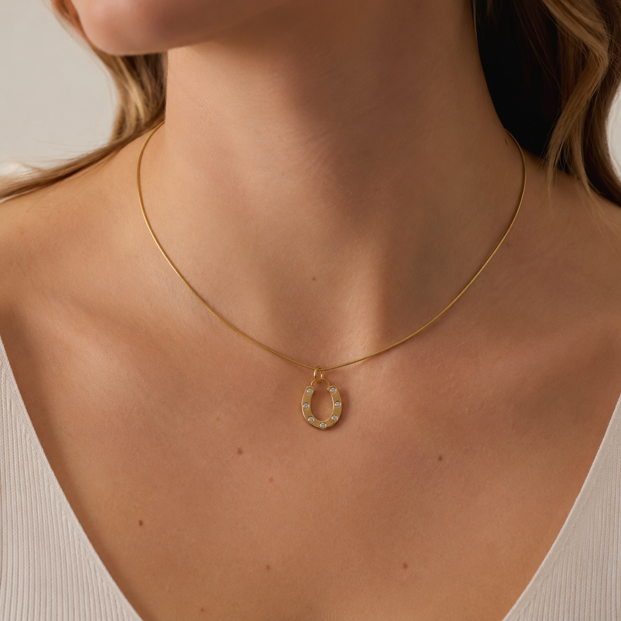 The Horseshoe CHARM worn as a pendant on a fine gold snake chain necklace, resting close to the neckline.