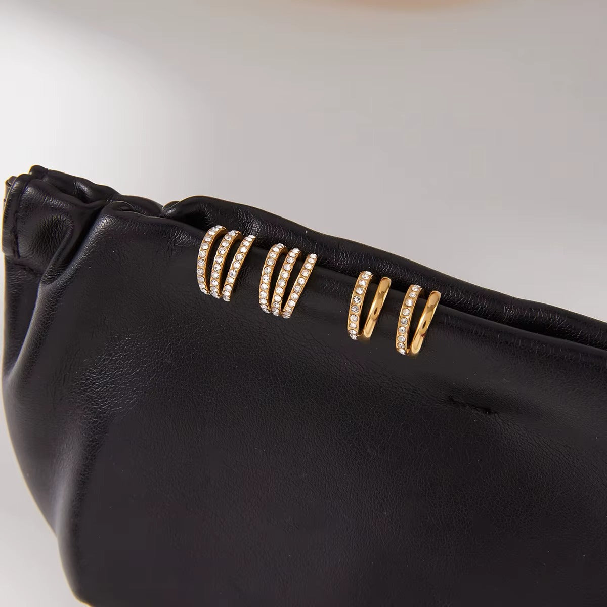 Two Hotline Ear Cuffs displayed on a black pouch beside a pair of pave crystal cuffs, showing the sleek double-band design up close.