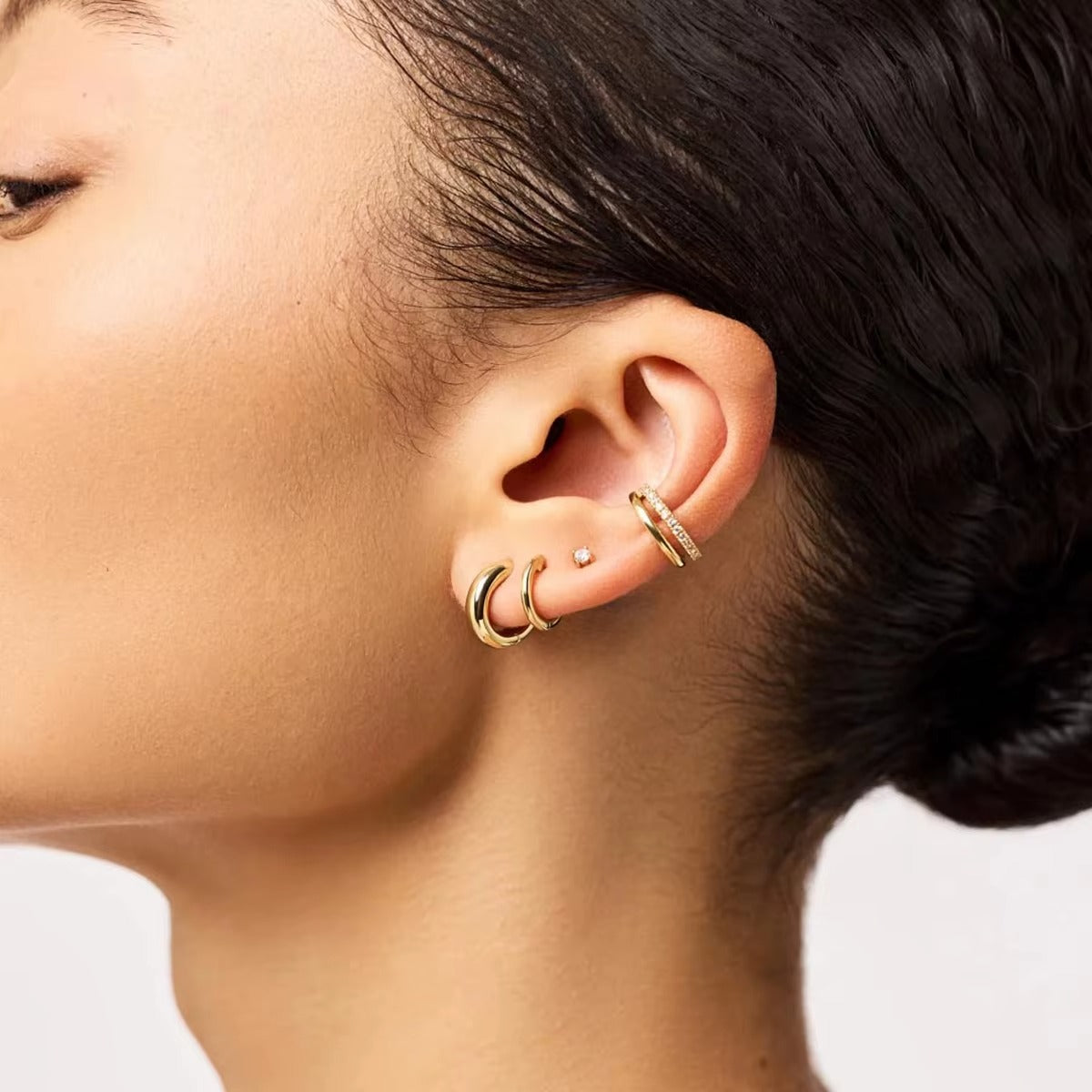 Hotline Ear Cuff worn on the cartilage above a pair of small gold hoops, completing a layered ear stack on a model with dark hair.