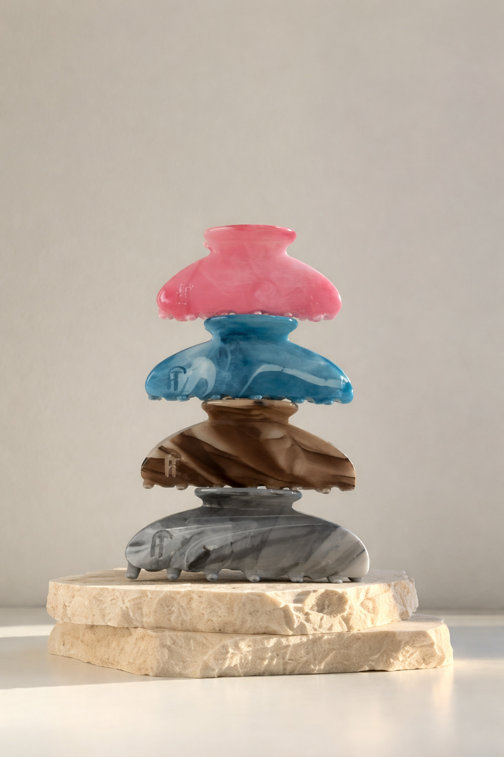 Ice Queen HAIR CLIP's pink, blue, brown and grey marbled claw clips stacked on a stone pedestal against a warm backdrop.