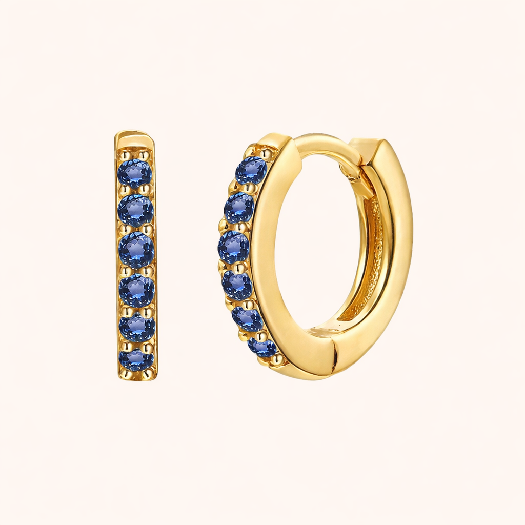 In a Dream Earrings in gold with sapphire-blue crystals, a huggie hoop set with six round stones in a row.