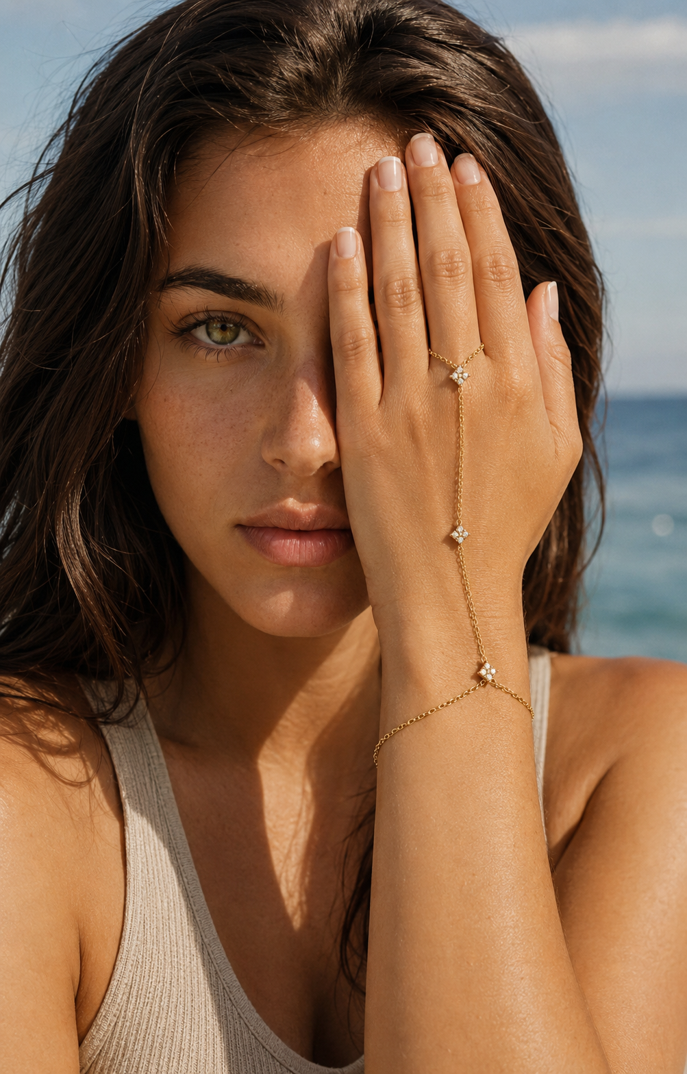 Insolite Hand Chain BRACELET worn on the hand with crystal stations catching light, model at the beach covering one eye.