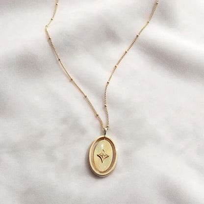 The Isyana NECKLACE in gold, the oval sunburst pendant with its diamond star accent styled on soft white fabric with its beaded chain.
