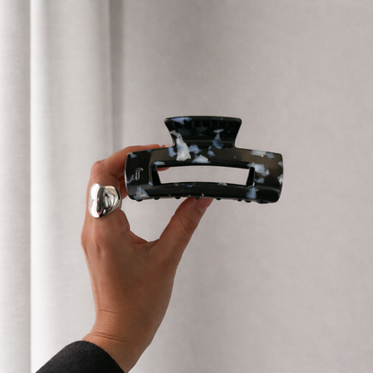 It Girl Medium HAIR CLIP's black speckled claw clip held up by hand against a curtain, styled with a silver ring.