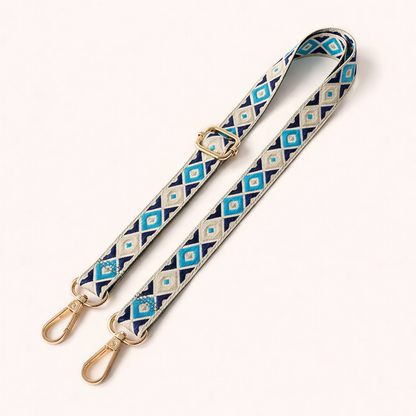 Woven Jetlag long phone strap in blue, navy, and cream diamond pattern, coiled flat with gold clasps.