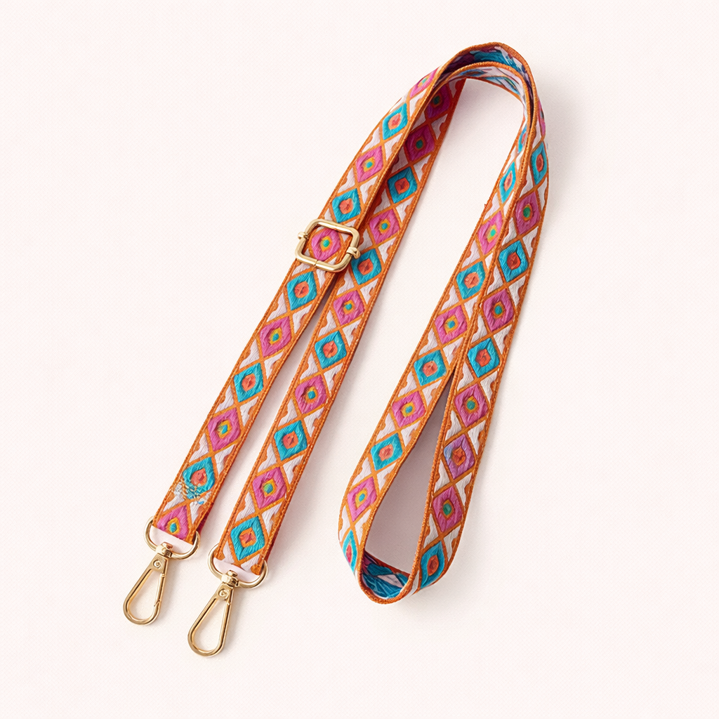 Woven Jetlag long phone strap in pink, teal, and orange diamond pattern, coiled flat with gold clasps.
