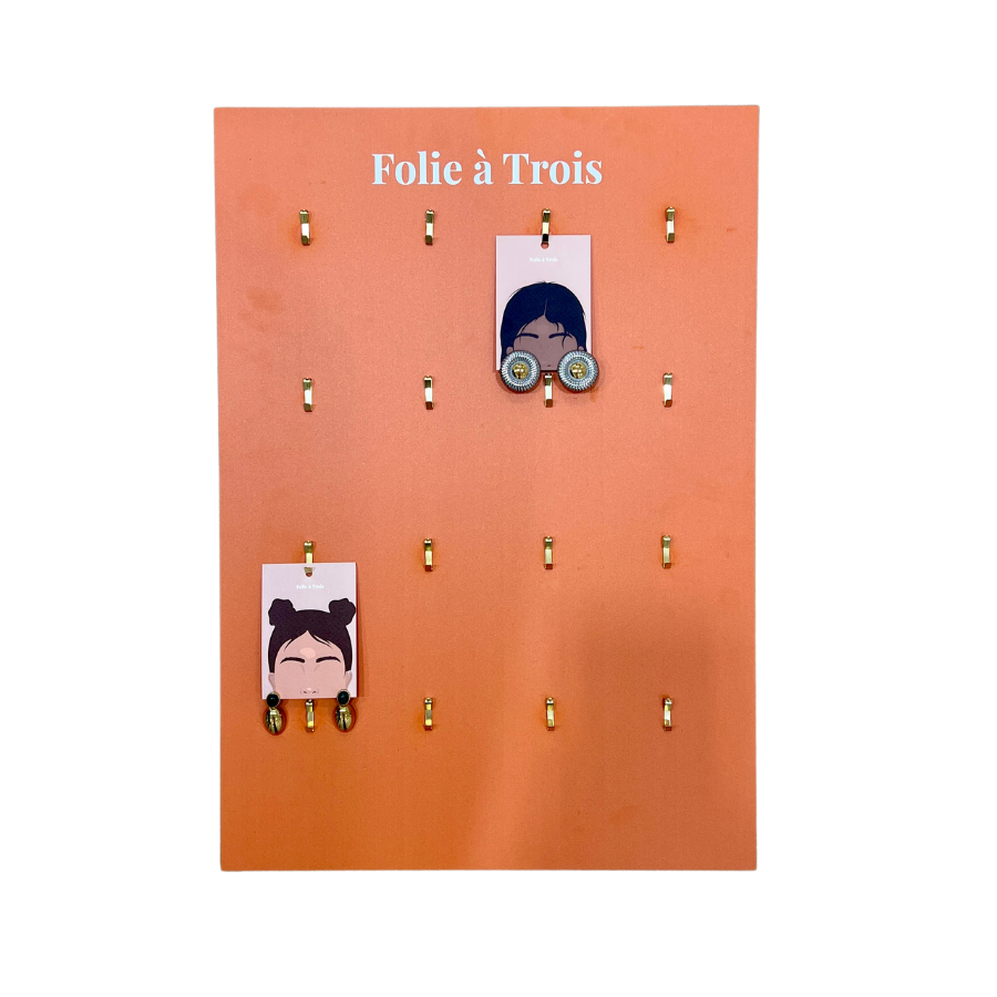 Terracotta Folie à Trois jewelry board with gold display hooks holding two illustrated face cards showing hoop earrings.