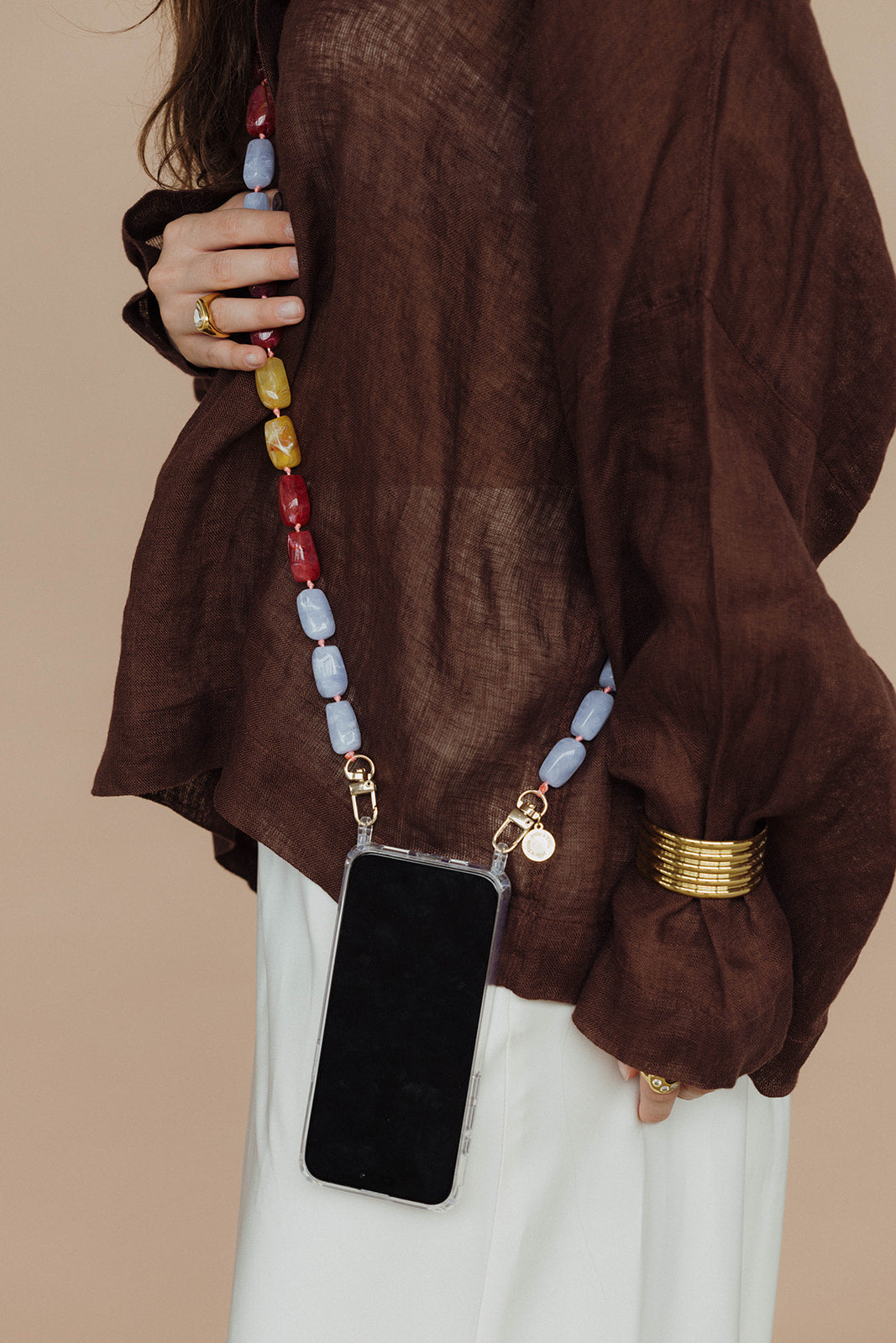 Close-up of a lavender, red, mustard, and steel blue bead phone chain attached to a phone, worn against a brown linen top.